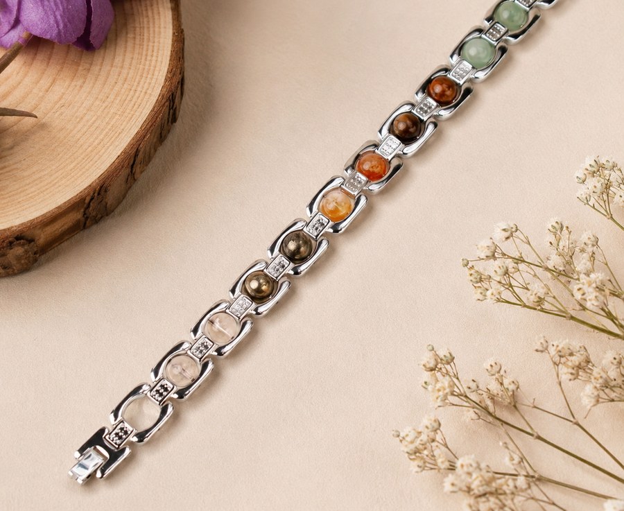 Men's energised Dhan Yog bracelet with polished silver links holding round clear quartz, rose quartz, pyrite, citrine, carnelian, tiger eye and green aventurine stones, on cream with a wood slice and dried flowers