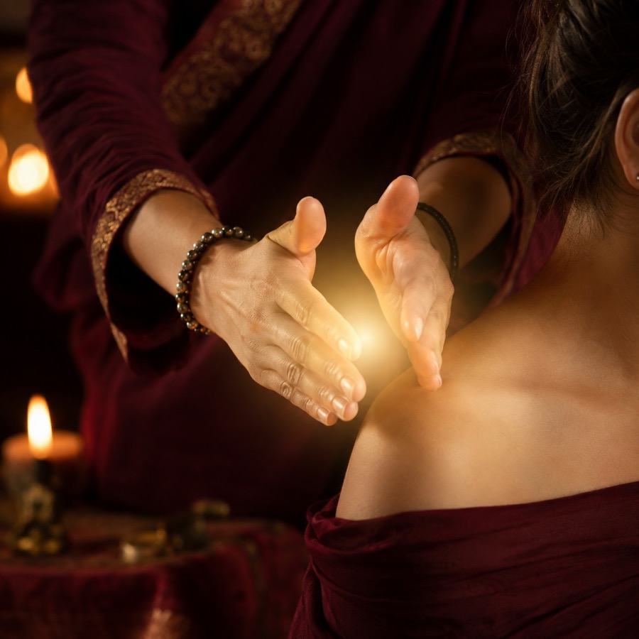 A healer's open hands held above a shoulder with warm golden light gathering between the palms